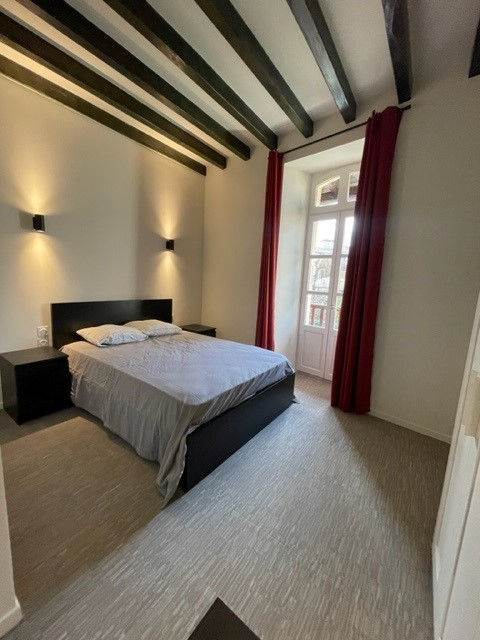 Chambre avec poutres apparentes, grand lit, bureau et porte-fenêtre à rideau rouge.